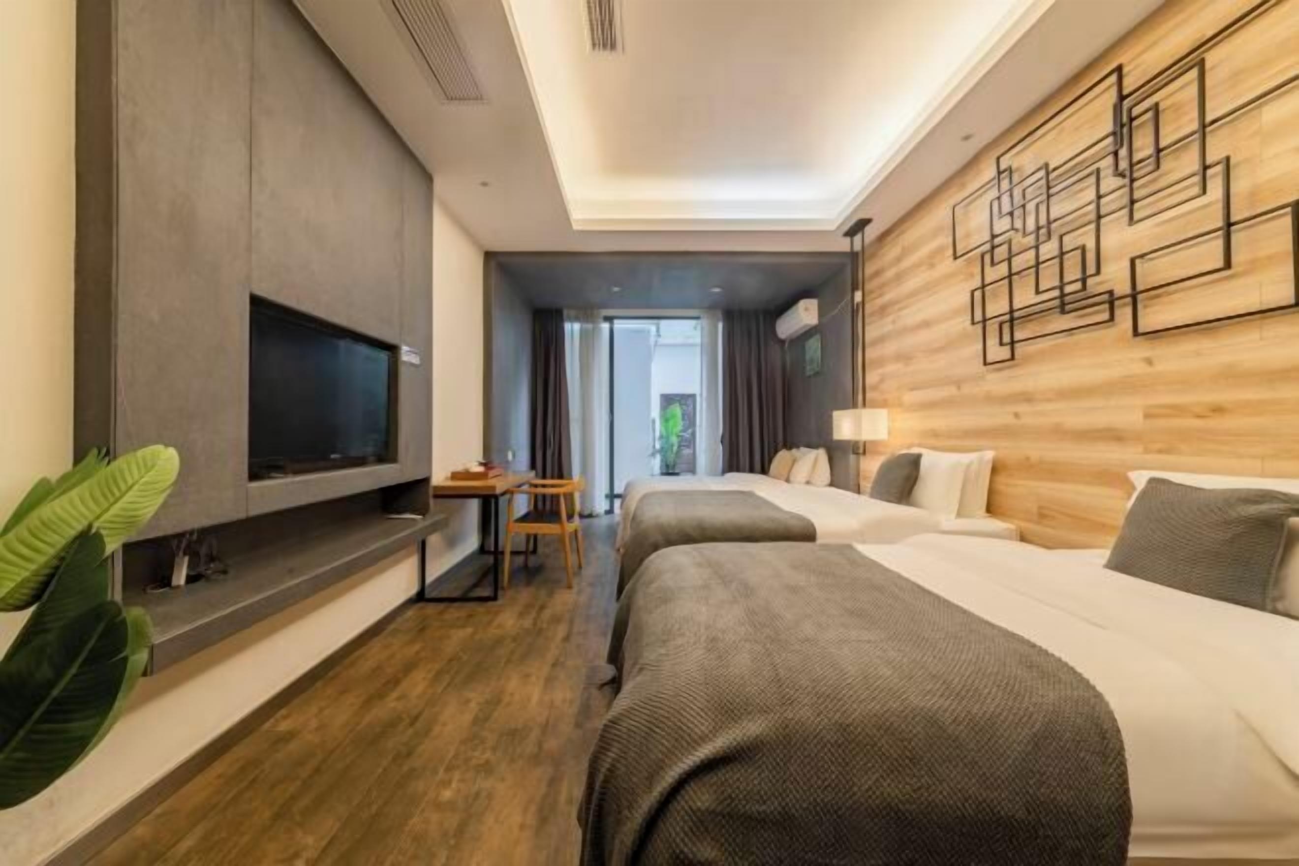 A modern hotel room with a flat-screen TV, two beds, a desk, and a large plant.