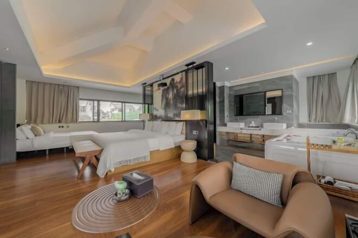 Une chambre d’hôtel moderne dotée d’un grand lit, d’un canapé, d’une table basse, d’une télévision et d’une salle de bain avec baignoire et lavabo.