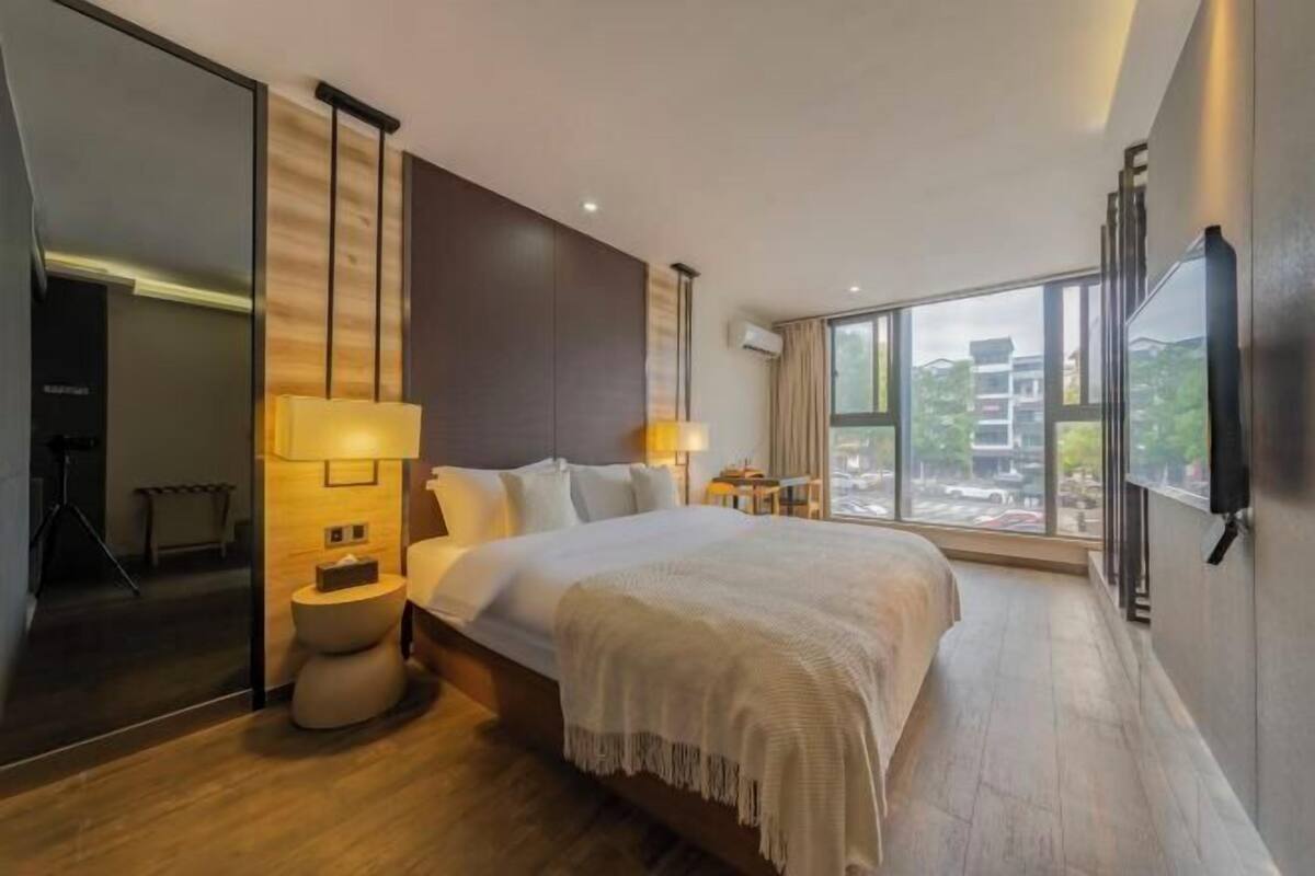 Une chambre d’hôtel moderne avec un grand lit, des lampes de chevet, une grande fenêtre et une vue sur la ville.