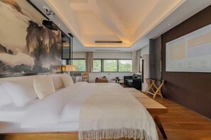 Una habitación de hotel moderna con una cama grande, un cuadro en la pared, un escritorio y vistas al exterior.