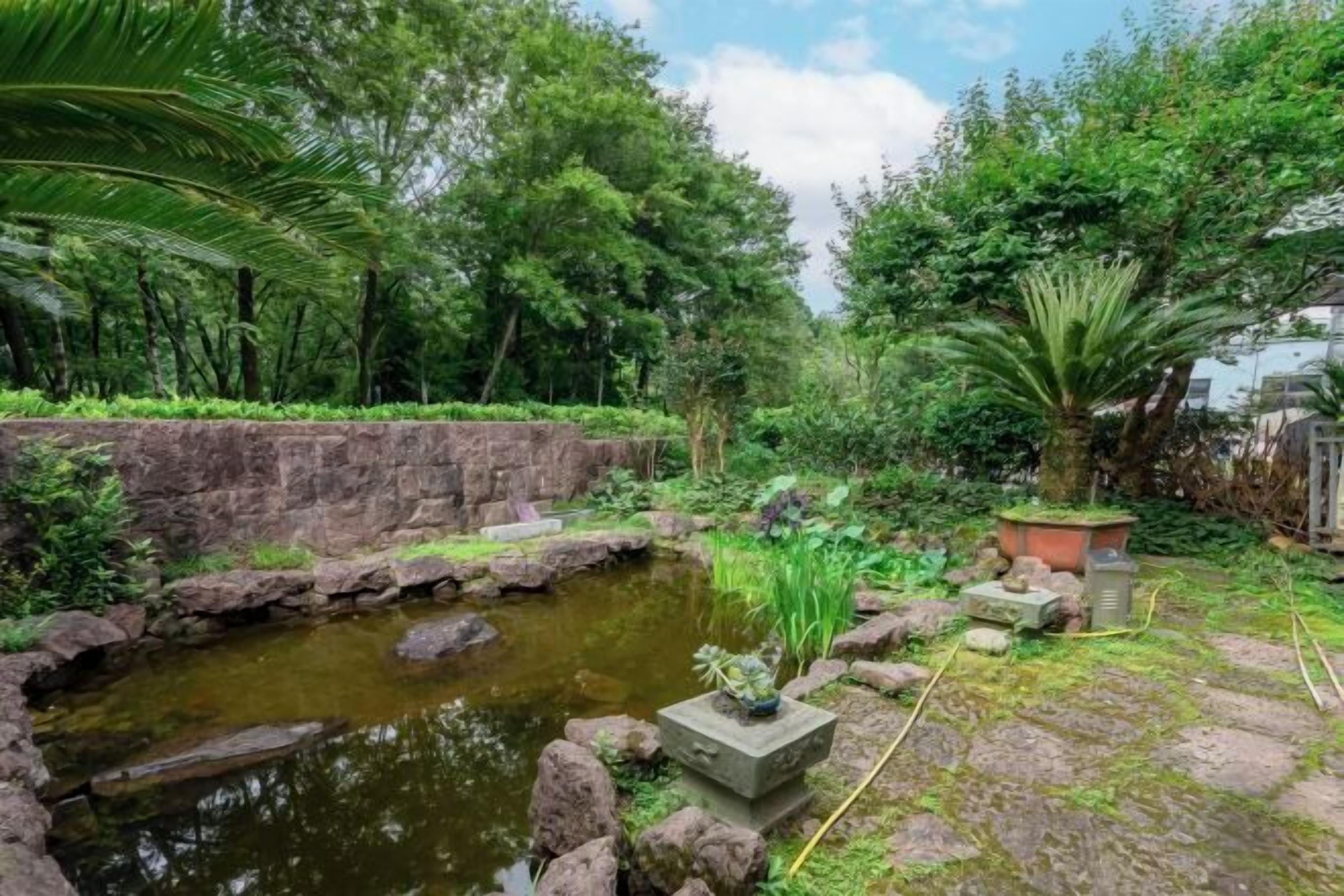 A serene garden with a pond, lush greenery, and a stone pathway.