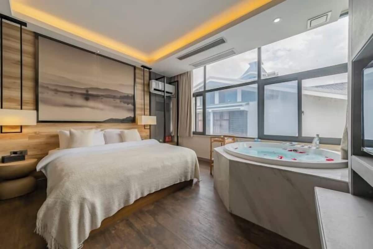 Une chambre à coucher avec un lit, une grande fenêtre, une baignoire et une vue sur l’extérieur.