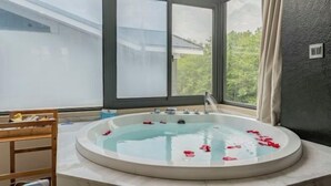 Spa-huone, jossa on suuri ikkuna, ruusunterälehdillä täytetty kylpyamme ja puinen penkki.