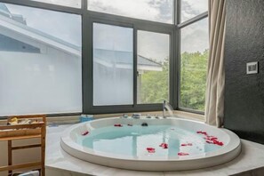 A spa room with a large window, a bathtub with rose petals, and a wooden bench. - Wuyishan Yuejiuqu Hotel (Zhuyu Wharf) (Wuyishan)