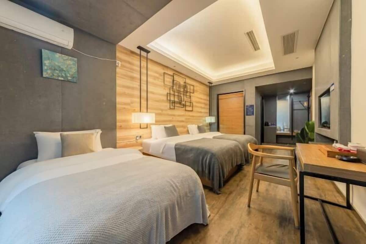 Une chambre d’hôtel avec deux lits, un bureau, une chaise, une lampe et un mur décoratif en bois.