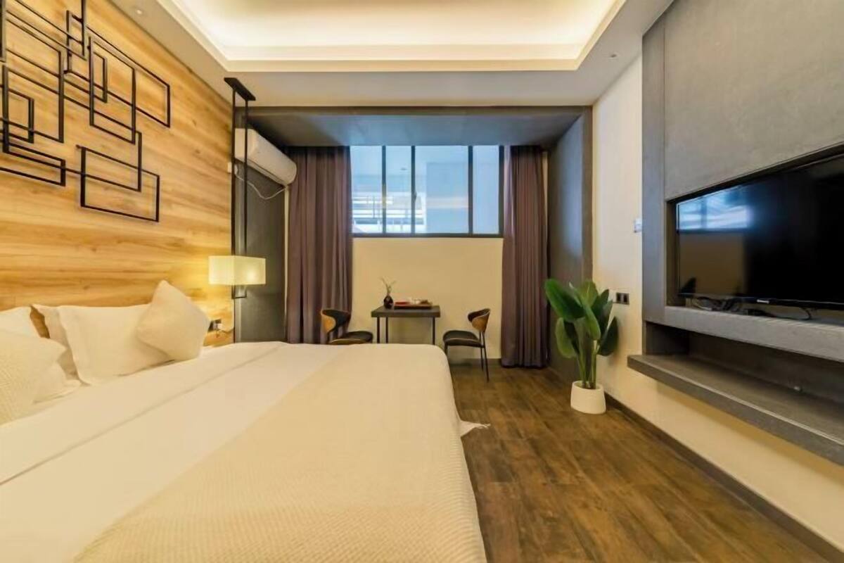 Une chambre d’hôtel avec un grand lit, une télévision, une petite table, une chaise et une plante en pot.