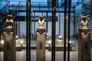 Tres estatuas de piedra sobre pedestales con inscripciones, una escalera y una barrera de vidrio.