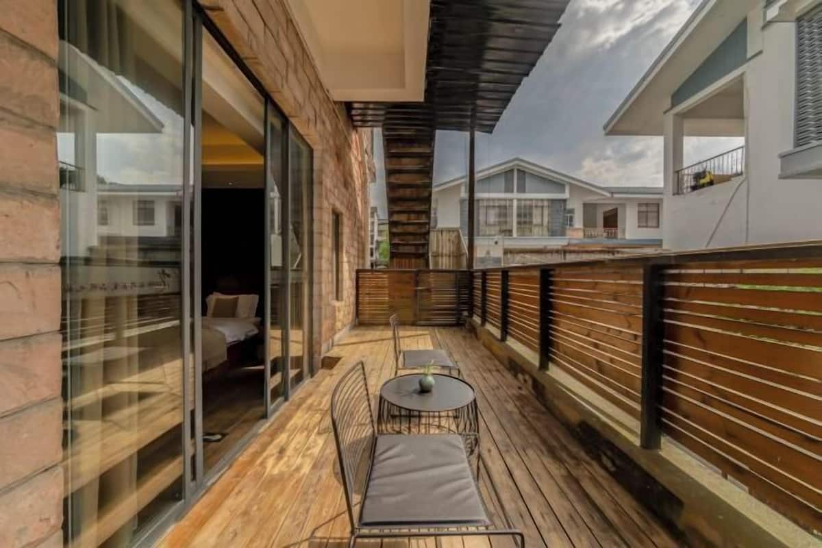 Une terrasse en bois avec une table et des chaises, une porte d’entrée en verre et une vue sur les bâtiments voisins.