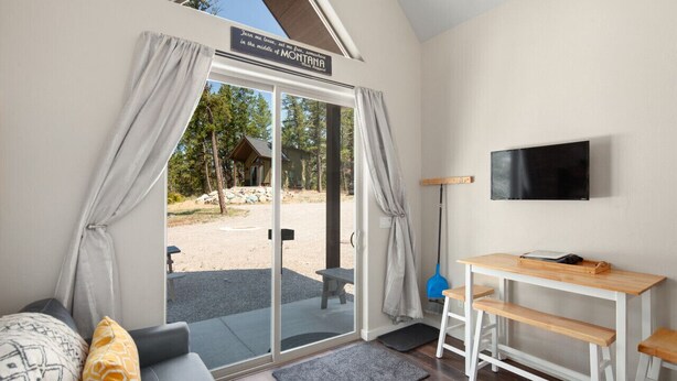 Une chambre moderne dotée d’une porte-fenêtre coulissante donnant sur un espace extérieur, avec un banc en bois, une petite table et un téléviseur fixé au mur.