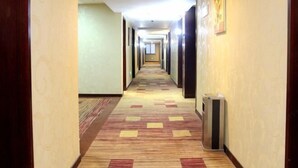 A hotel corridor with a carpeted floor, doors on both sides, and a trash bin on the right. - Yong Xing Holiday Hotel (Zhoushan)