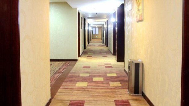 Pasillo de hotel con piso alfombrado, puertas a ambos lados y un bote de basura a la derecha.