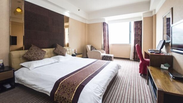 A hotel room with a large bed, a desk, a chair, a TV, and a window. - Yong Xing Holiday Hotel (Zhoushan)
