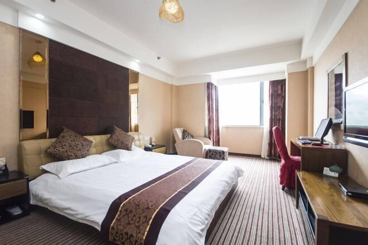 Hotelkamer met groot bed, bureau, stoel, televisie en raam.