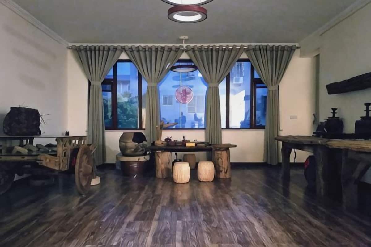 A room with a wooden floor, a table with chairs, a window with curtains, and a hanging light fixture.