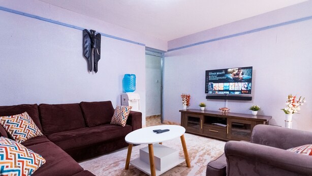 Ein Wohnzimmer mit einem braunen Sofa, einem weißen Couchtisch und einem an der Wand befestigten Fernseher.