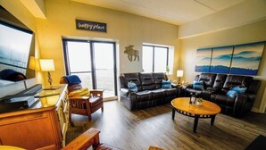 A cozy living room with a fireplace, leather sofas, a wooden coffee table, and a large window offering a view. - Altitude Adjustment - King bed, Gig-Speed Internet, Mountain View, Ski (Sugar Mountain)