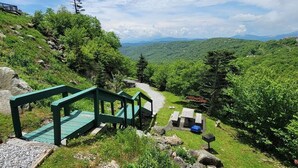 A green wooden staircase leading to a viewing platform with benches and a picnic table, surrounded by lush greenery and rocky terrain. - Altitude Adjustment - King bed, Gig-Speed Internet, Mountain View, Ski (Sugar Mountain)