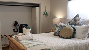Un dormitorio con cama, ventilador de techo, mesita de noche con lámpara y ventana con persianas.