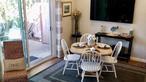 Un comedor con mesa y sillas, un televisor montado en la pared y un ventanal corredizo que da a un espacio exterior.