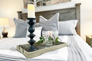 Un lit bien fait, sur lequel se trouve un plateau avec une bougie, des verres et un petit vase.