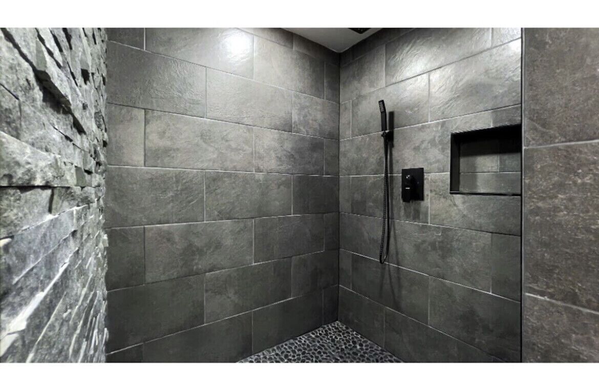 A shower area with grey tiles and a textured wall.