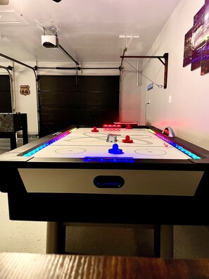 Een tafelvoetbaltafel met LED-verlichting, een projector bevestigd aan het plafond en een 'Route 66' bord aan de muur.