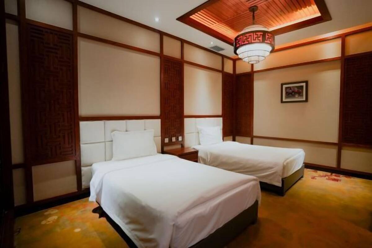 A hotel room with two beds, wooden paneling, a ceiling light fixture, and a framed picture on the wall.