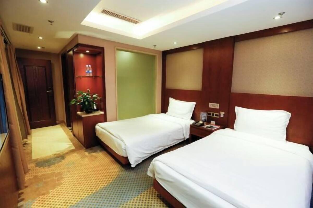 A hotel room with two beds, a small seating area with a plant, and a door leading to another room.