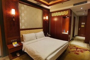 A hotel room with a large bed, wooden headboard, a nightstand, a wardrobe, and a decorative wall panel. - Kunming Shuitian Hot Spring Hotel (Kunming)