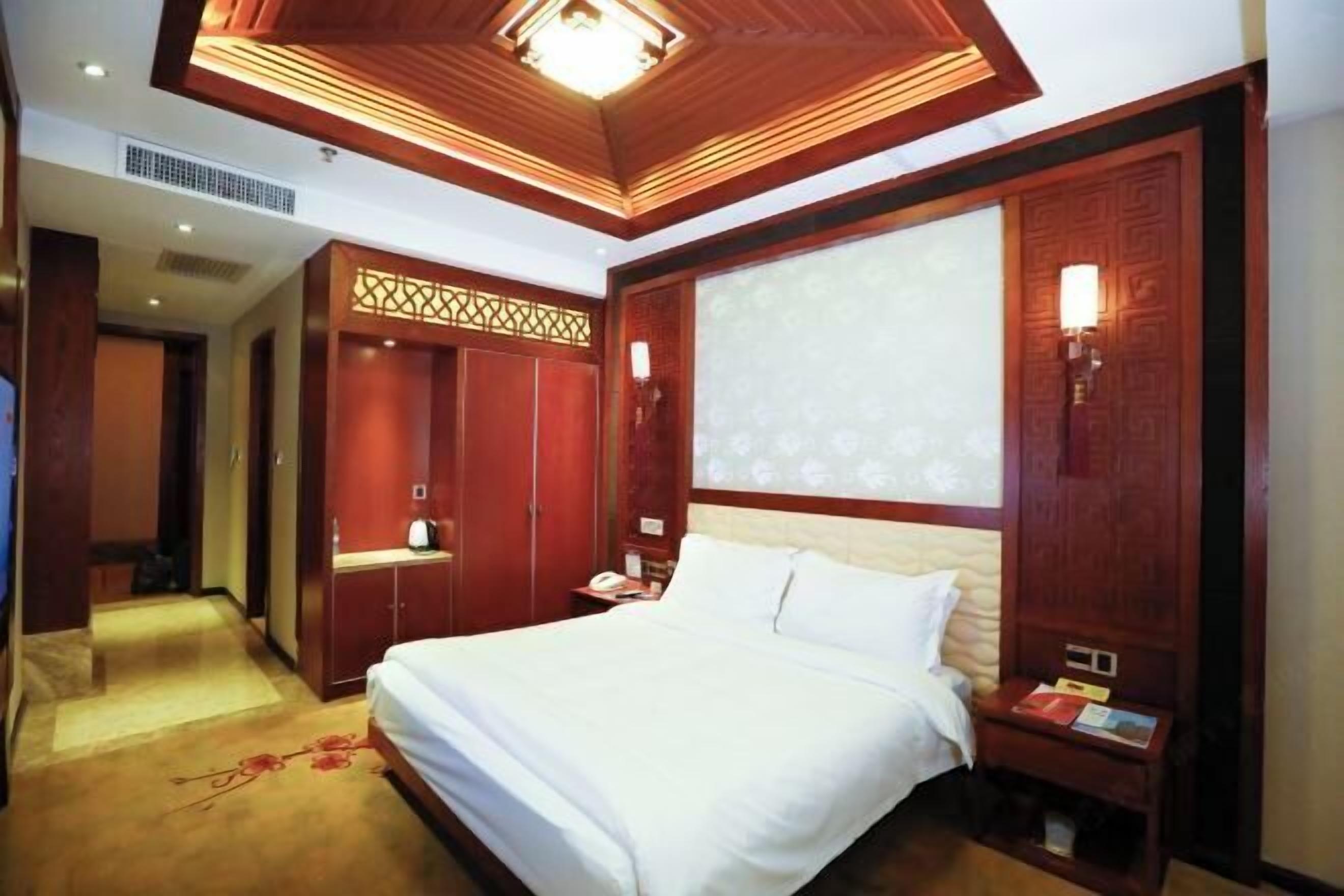 Ein Hotelzimmer mit einem großen Bett, einem Holzschrank und einer dekorativen Decke.