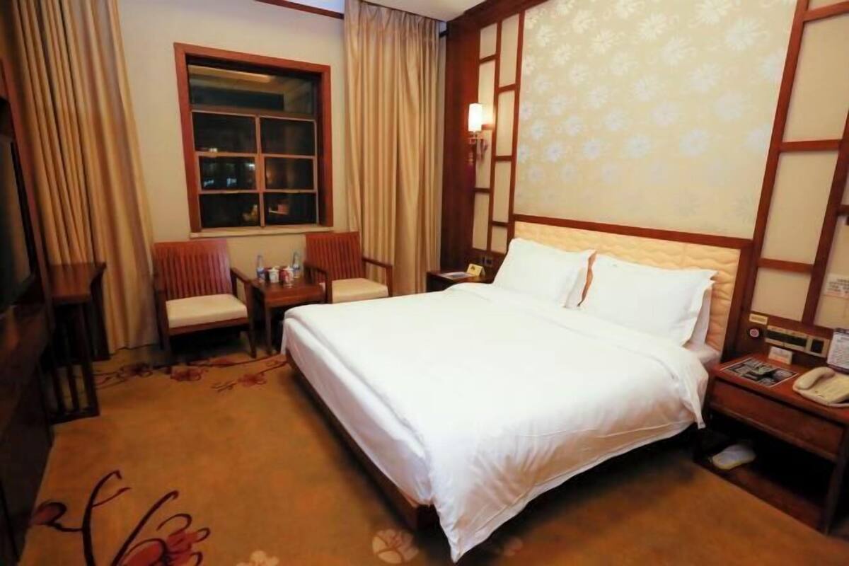 A hotel room with a bed, a chair, a nightstand, a window, and a curtain.