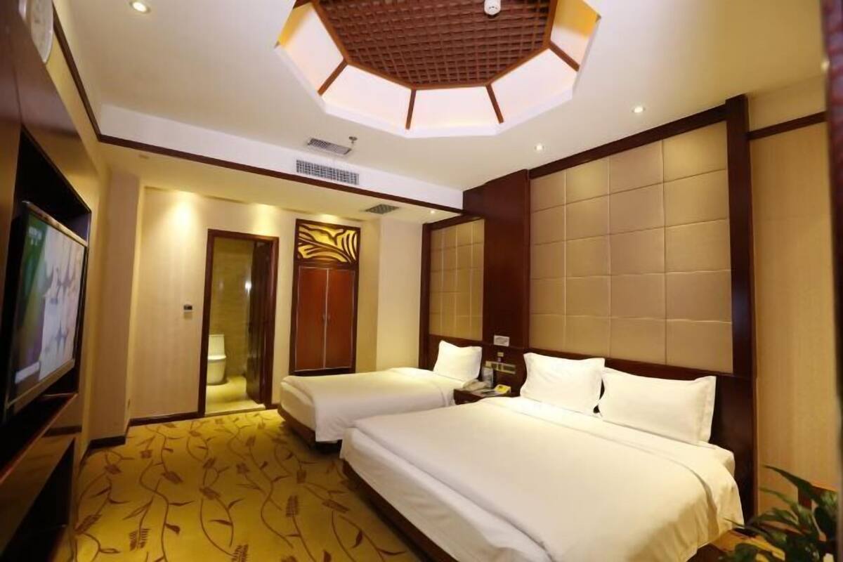 A hotel room with two beds, a television, and a ceiling with a geometric design.