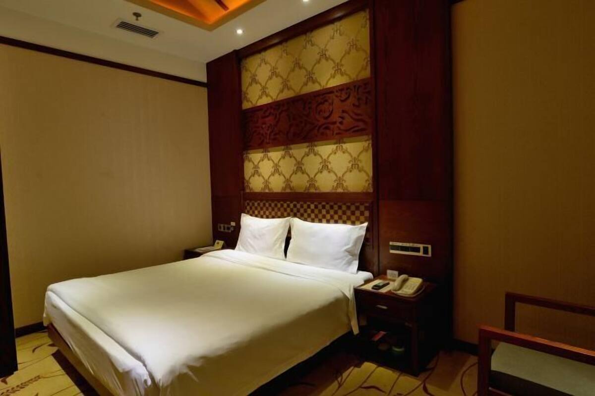 A hotel room with a large bed, a wooden headboard with intricate patterns, a bedside table with a telephone, and a chair.
