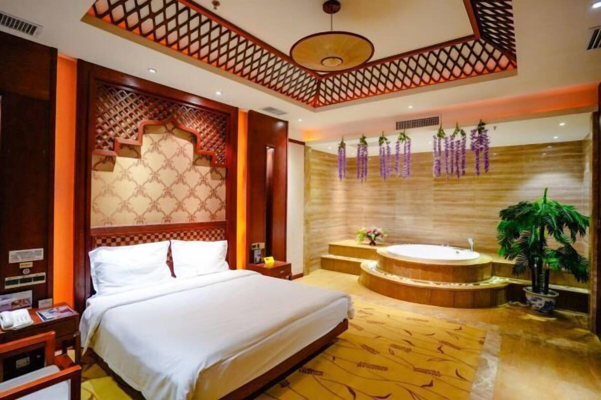 A hotel room with a large bed, a round bathtub, and a wall-mounted sink.
