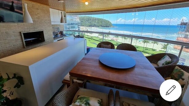 A modern kitchen with a large island, a dining area with wicker chairs, and a view of the ocean.