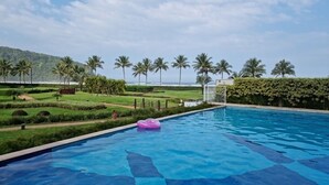 A swimming pool with a pink float, surrounded by palm trees and a view of the ocean.