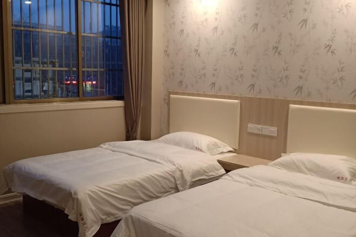 A hotel room with two single beds, a window with a view of the street, and a wall with a bamboo pattern.