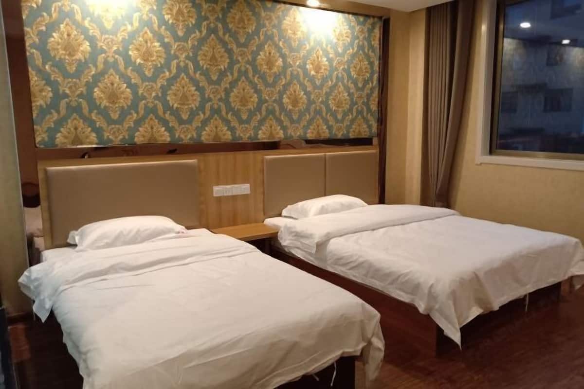 A hotel room with two single beds, a wooden headboard, and a patterned wallpaper.