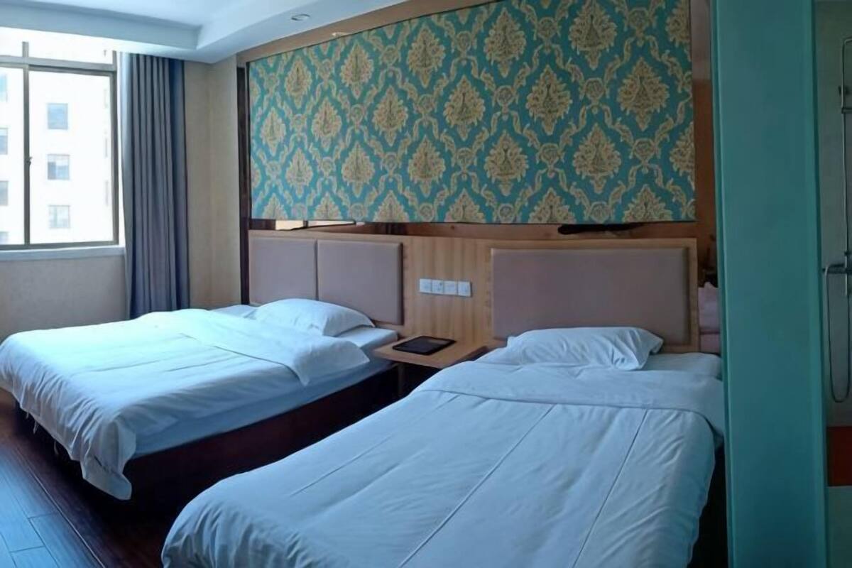 A hotel room with two beds, a window with curtains, a patterned wall, and a wooden headboard.
