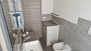 Un bagno moderno con un lavandino bianco, un bidet e uno specchio. Sono presenti articoli da toilette su uno scaffale e un porta asciugamani.
