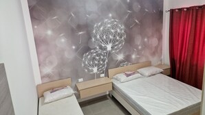 A bedroom with two beds, a wall mural of a tree, and a red curtain.