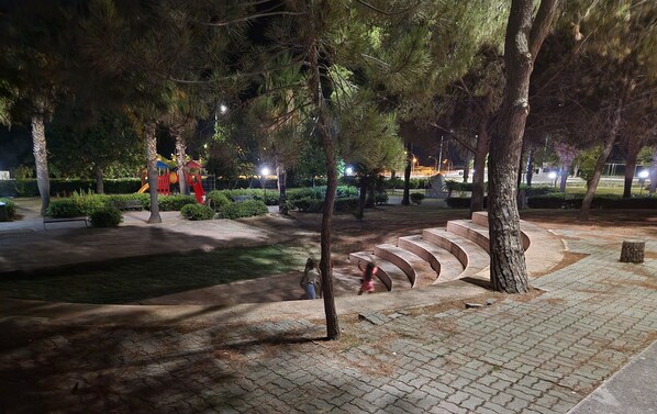 A nighttime park with a playground, paved pathways, and trees.