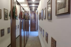 Un pasillo con cuadros enmarcados en las paredes, una puerta de madera y una escalera al fondo.