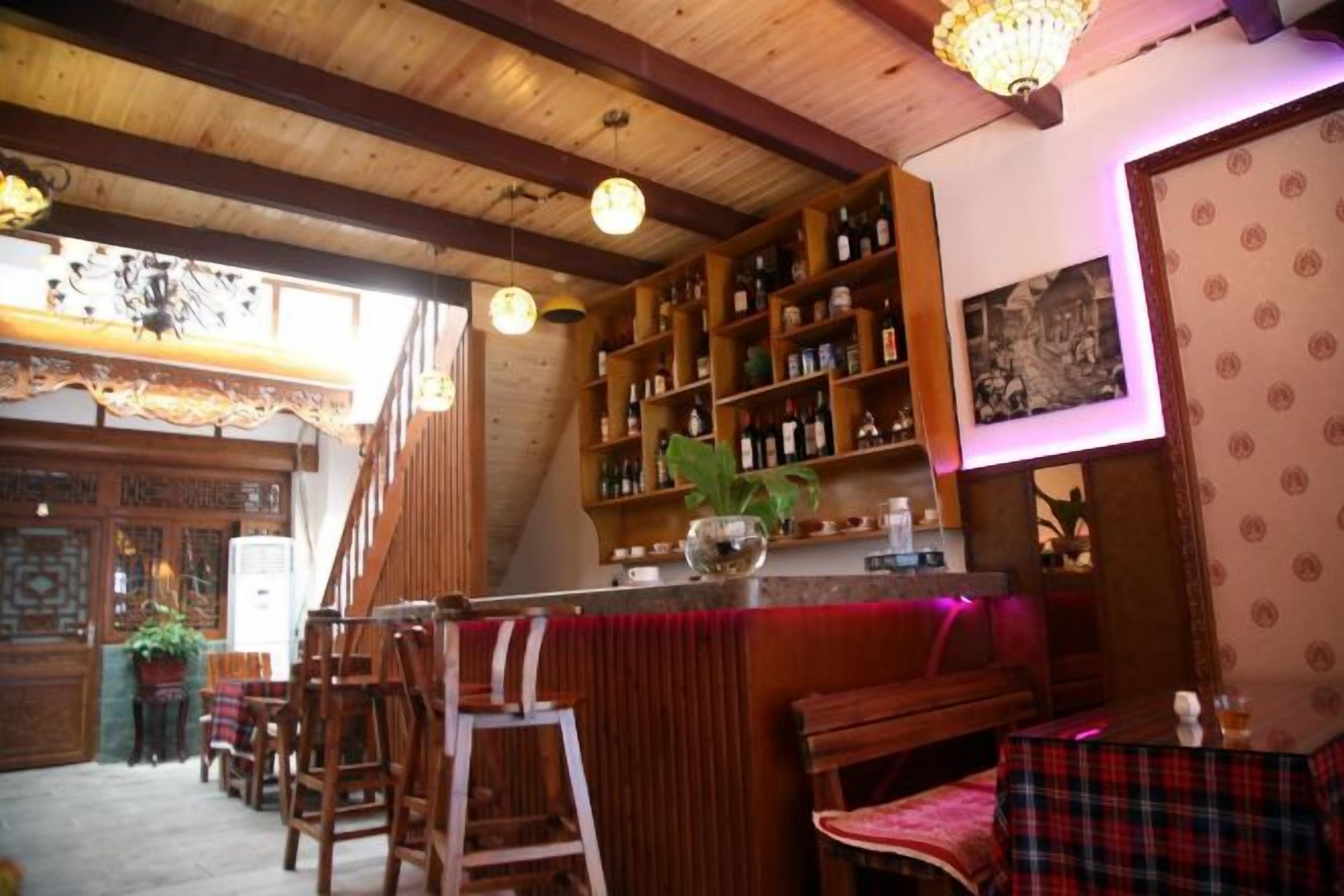 A bar area with wooden furniture, a bookshelf with bottles, and a patterned wall.