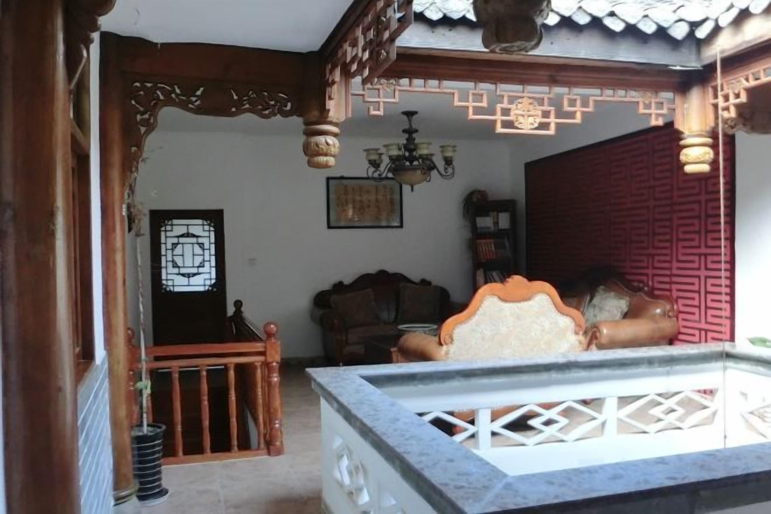 Una habitación tradicional con techo de madera, cama con cabecera blanca, separador rojo y candelabro.
