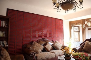 A living room with a red patterned wall, a brown leather sofa, and a chandelier.