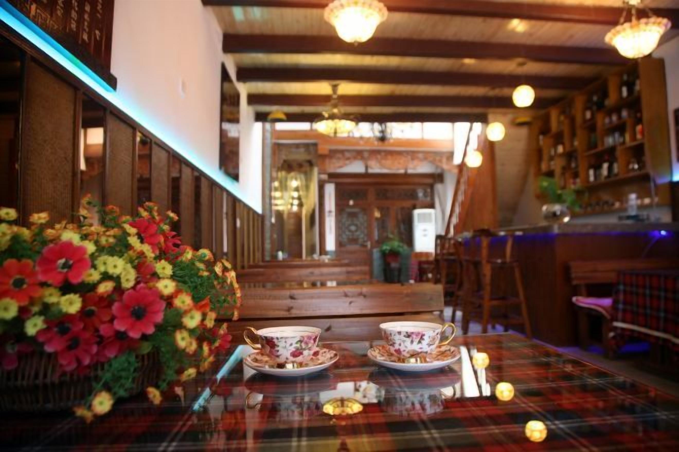 A restaurant interior with a table set for two, a floral centerpiece, and a bar area in the background.