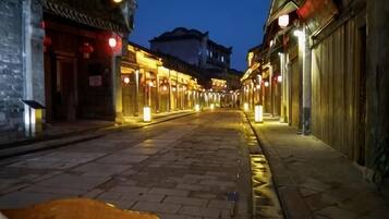 A narrow street with traditional architecture, illuminated by warm lighting, and a clear sky.