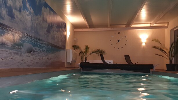 An indoor swimming pool with clear water, a mural of a beach scene, and two wall-mounted lights.