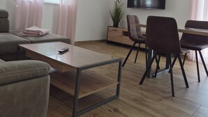 A modern living room with a sofa, a coffee table, a TV, and a dining area with chairs and a table.
